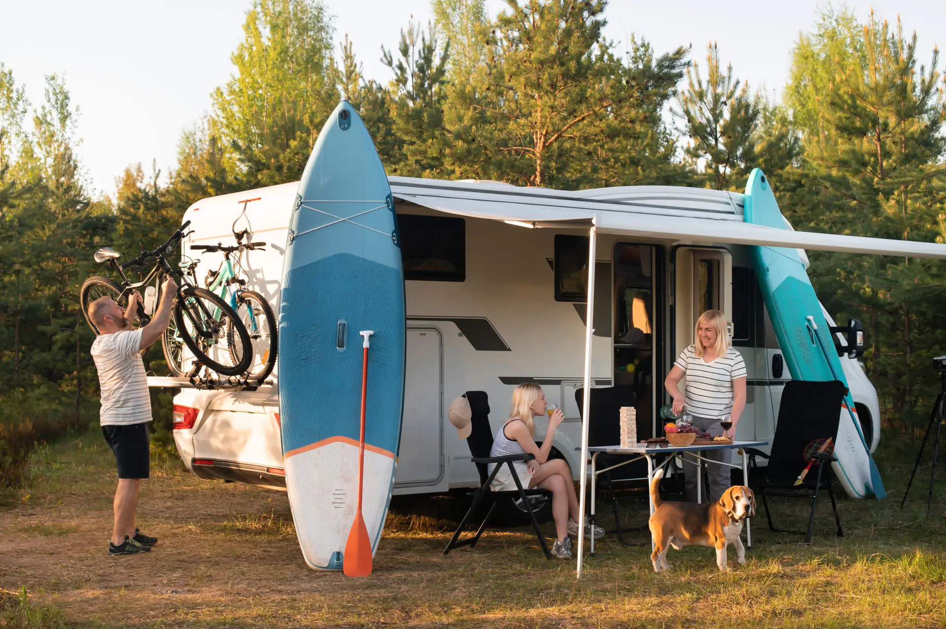A happy family is resting nearby near their motorhome in the forest.
