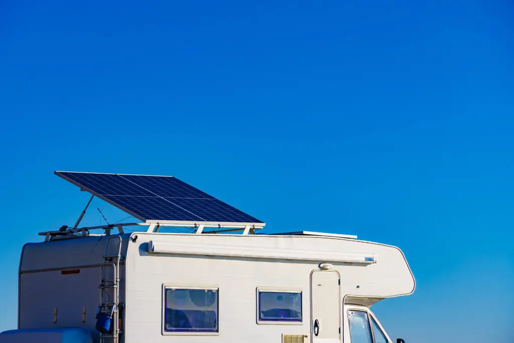 Camper rv with tilt solar photovoltaic panels on roof camping on nature in wintertime. Blue sky with copy space.